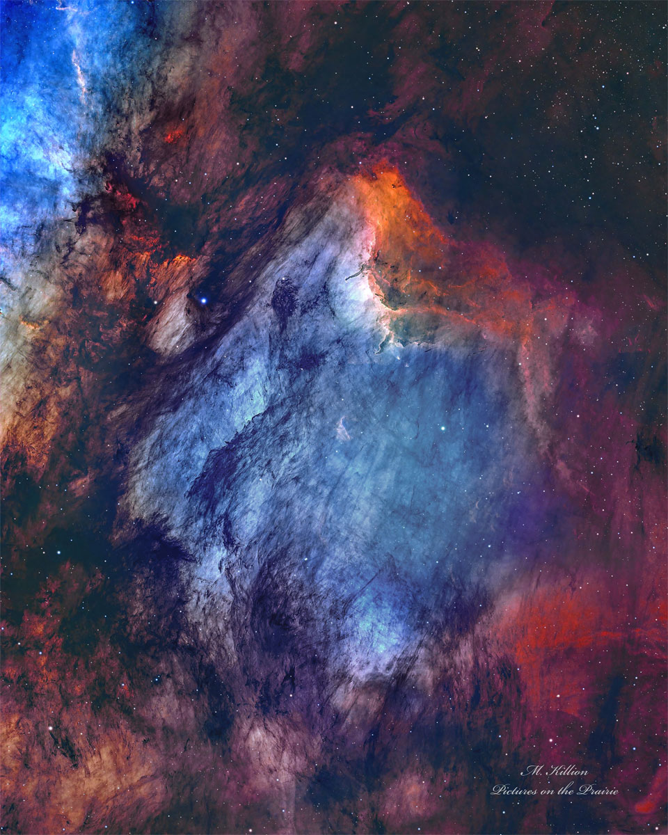 鹈鹕星云特写：蓝白色气体丝缕居中如羽，砖红发射云铺底，上缘一道亮橙色电离前沿