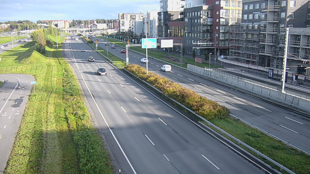 坦佩雷湖滨路傍晚：多云天光下的多车道马路，右侧红砖公寓楼与工地，左侧绿坡自行车道