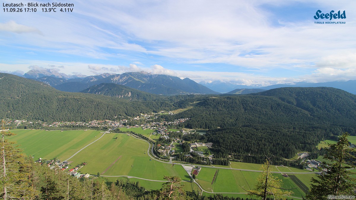 勒塔施高原全景：绿茵草甸铺向谷底小镇，松林与层叠远山在晴空下