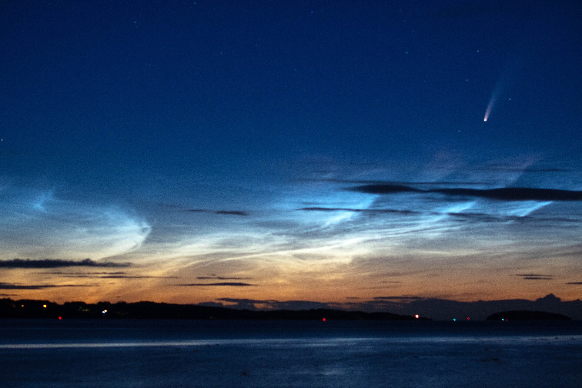 NEOWISE 彗星与夜光云：深蓝夜空中彗星拖着尾巴悬于右上，银蓝色夜光云如波浪铺满海天之间